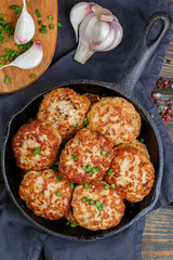 Juicy delicious chicken or Turkey cutlets with garlic and green onions in a cast iron pan on a dark wooden table. Rustic style. Selective focus, top view