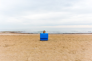Fototapeta na wymiar Woman with blue suitcase on the beach. Funny picture, joke and humor concept.
