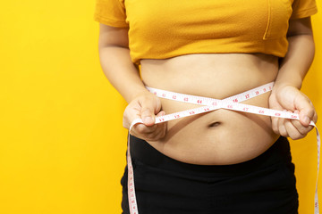 fat woman check out body overweight abdomen she belly with in hand measuring tape for yellow or obesity background. Weight loss concept. - obrazy, fototapety, plakaty