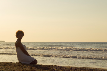 Fototapeta na wymiar African American black woman thinking on the beach in the sunrise with white dress.