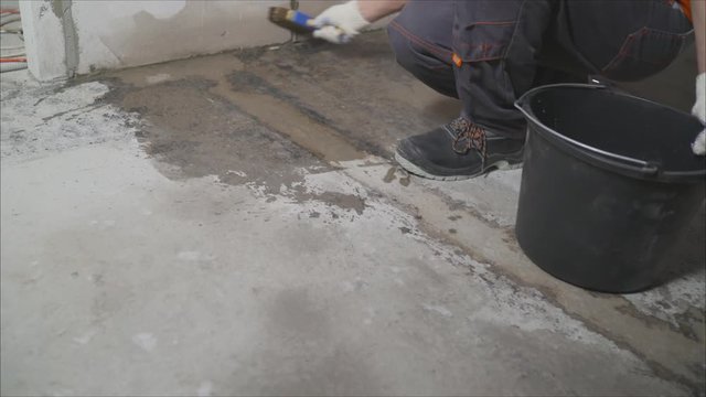 Worker smears concrete floor with water for processing. Waterproofing concrete floor. The worker makes a preliminary step before waterproofing the floor.