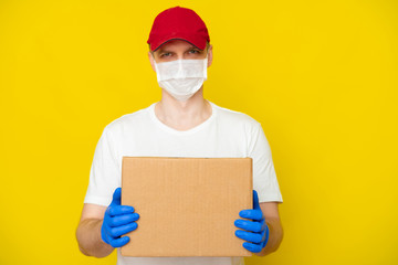 Delivery man in red cap white t-shirt uniform face medical mask gloves hold empty cardboard box on yellow studio background. Service coronavirus. Online shopping. mock up.