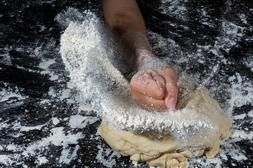 Fist of a child impacting on flour kneaded in a black surface full of flour dust