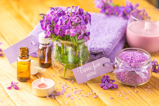 Time for you text phrase on label sticker. Spa still life with violet oil, towel, violaceous bath salt in glass jar and perfumed candle on natural wood table surface