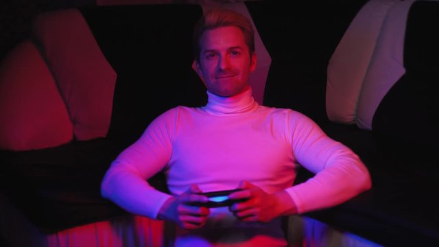 a bright young man plays a video game, is upset, is crazy about being angry that he lost against a sofa in a blue-red background