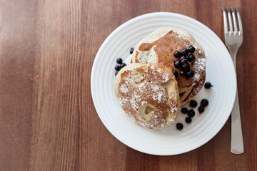 pancakes with berries and powdered sugar in a white plate are on the table