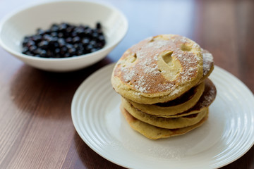 pancakes with berries and powdered sugar in a white plate are on the table