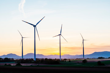 4 wind turbines stand in a small wind farm in the Rhine valley near Landau in front of the silhouette of the Palatinate Forest.