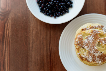 pancakes with berries and powdered sugar in a white plate are on the table