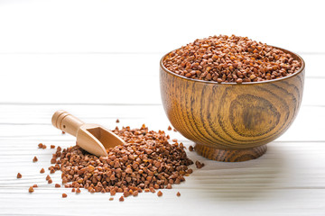 brown buckwheat grains in wooden bowl on isolated white background Healthy food, superfood concept