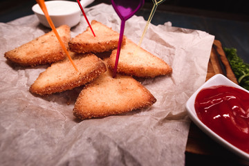 Appetizing fried cheese with sauce on a wooden tray. Studio photography of food in the cooking industry, dark background