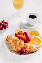 Breakfast with croissants, coffee, peaches, raspberries and orange juice