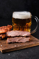 Cutted pork ribs and big glass of beer on cutting board on dark