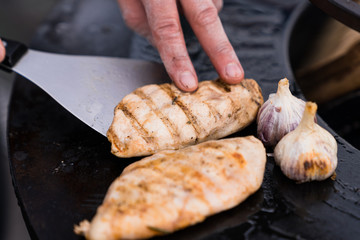 Mans hands turn over chicken and garlic on a grill