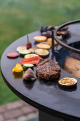Beef steak and sliced vegetables on a round grill surface.