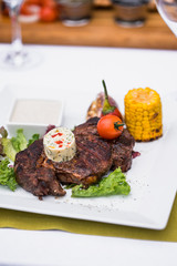 Beef steak on a plate with butter on it, corn and cherry tomatoes and white sous.