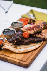Kebab meat and grilled chicken breasts and cherry tomatoes on a white plate with souses.