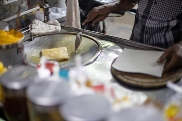 Fototapeta na wymiar Hands of street vendor cooking Thai style sweet roti bread on steel roti pan or big flat frying pan. Enjoy Thailand’s street food