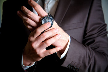 One young man puts a black watch on his wrist. A man in a black suit in a dark room.