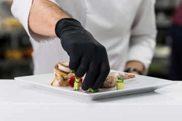 Chef in black gloves serving plate with meal , vegetables on a plate.
