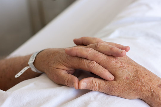 Elderly man's clasped hands wearing hospital identity bracelet