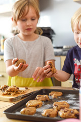 Kids making cookies in kitchen placing dough on tray for cooking at home