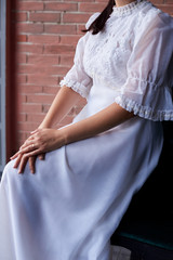 Close-up picture of bride's hands, wearing white tender dress, in front of brick wall in the morning. Wedding day decorations details.