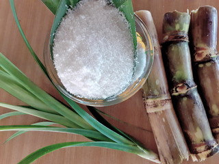 Refined sugar in a glass cup, with fresh sugar cane stems separate, on the old wooden floor, next...