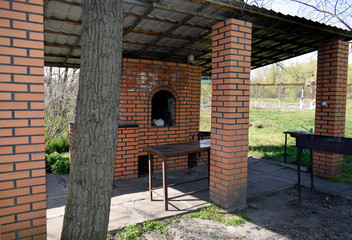 Oven, smokehouse and barbecue made of red stone. Construction with a roof for a barbecue in nature.