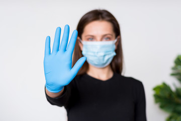 Young woman in medical mask and gloves shows stop sign by her hand.