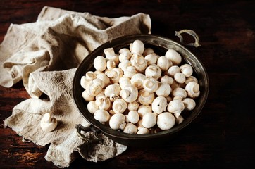 Fresh raw champignons in an iron bowl on a dark wooden table, rustic style