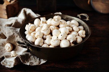 Fresh raw champignons in an iron bowl on a dark wooden table, rustic style