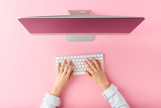 Office desktop concept. Woman&rsquo;s hands working on computer on pink background. Top view