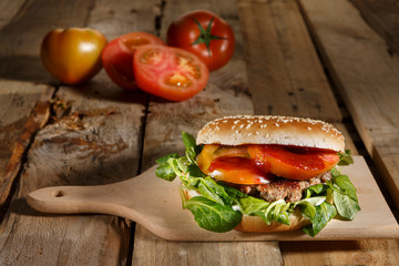 Invitante Hamburger proposto in un tagliere di legno in un tavolo di legno, sullo sfondo pomodori tagliati e interi