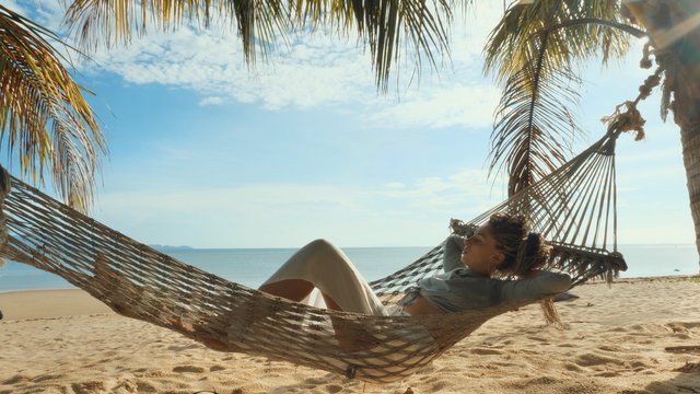 Relaxed woman swinging in a hammock at sand beach of Thailand