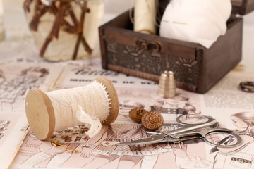 Still life retro sewing box and accesories, spool, pins, needles, buttons and scissors on sewing magazine