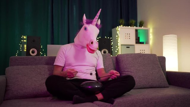 a man in a mask unicorn sits at home and plays on the hapi drum