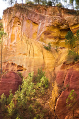 Vertical picture of ochre Trail in Roussillon, Sentier des Ocres, hiking path in natural colorful area of red and yellow cliffs in ocher pigment quarry surrounded by forest in Provence, France