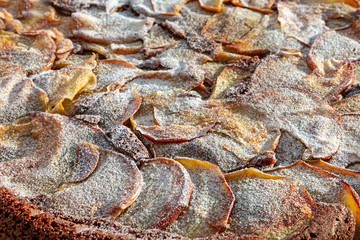 Freshly baked apple pie with slices of apples sprinkled with icing sugar in the background. Close-up.
