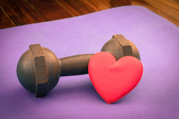 Metal dumbbell with red heart on yoga mat.