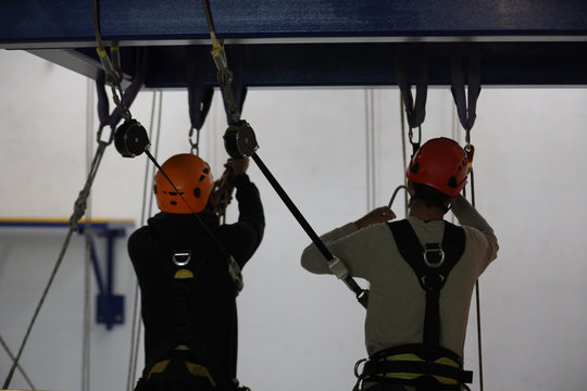 Abseiler maintenance wearing orange safety fall protection helmet working at heights using an inertia reel shock absorber lanyard as fall arrest connecting into body harness hook prior to used 