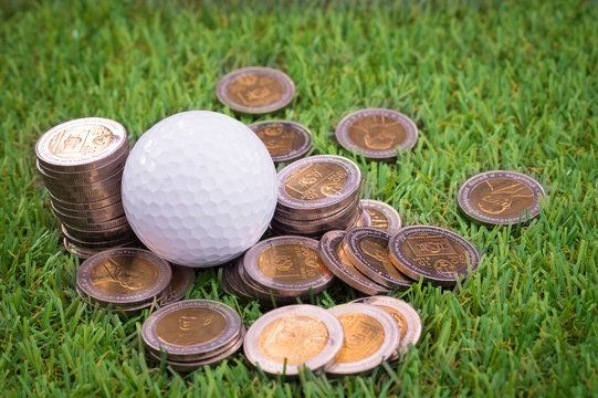 Golf ball with golden coins on green grass.