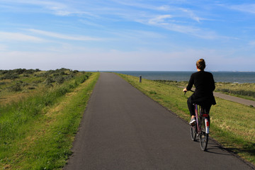 Fahrradfahrerin auf einem leeren Deichweg in Zeeland