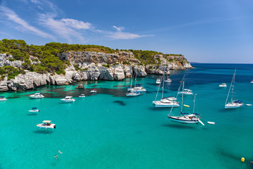 Panoramic view of the beautiful Macarella bay with many boats on the island of Menorca in Spain. - obrazy, fototapety, plakaty