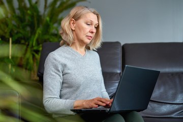 Woman on a sofa at home concentrating as she works on a laptop