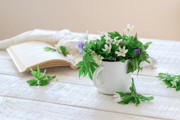 A bouquet of white wood anemones and a book on a white wooden table