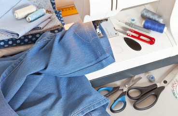 Needlework and sewing. Hemming jeans on sewing machine. Processing the bottom of denim pants. Accessories for sew. Close-up, top view