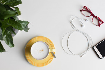 Flat lay of mobile phone, headphones, glasses and cappuccino