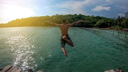Men wearing shorts swimming trunks Jump off the bridge into the blue sea A fun way of life in the summer On an island in Thailand.jump in mid air on sunny day summer at diving holiday Travel vacation