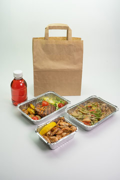 Delicious meals with daily delivery. Fitness food, vegetables, meat and Morse, compote in foil boxes, Cutlery in a paper bag on a white background.